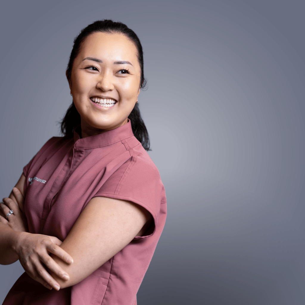 Smiling woman with arms crossed wearing pink medical scrub top