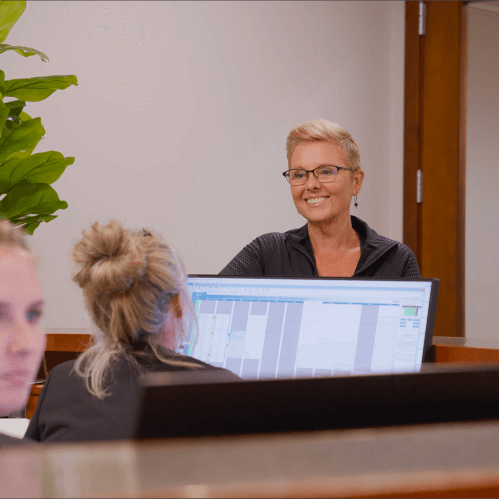 Smiling staff member with glasses at a front desk computer