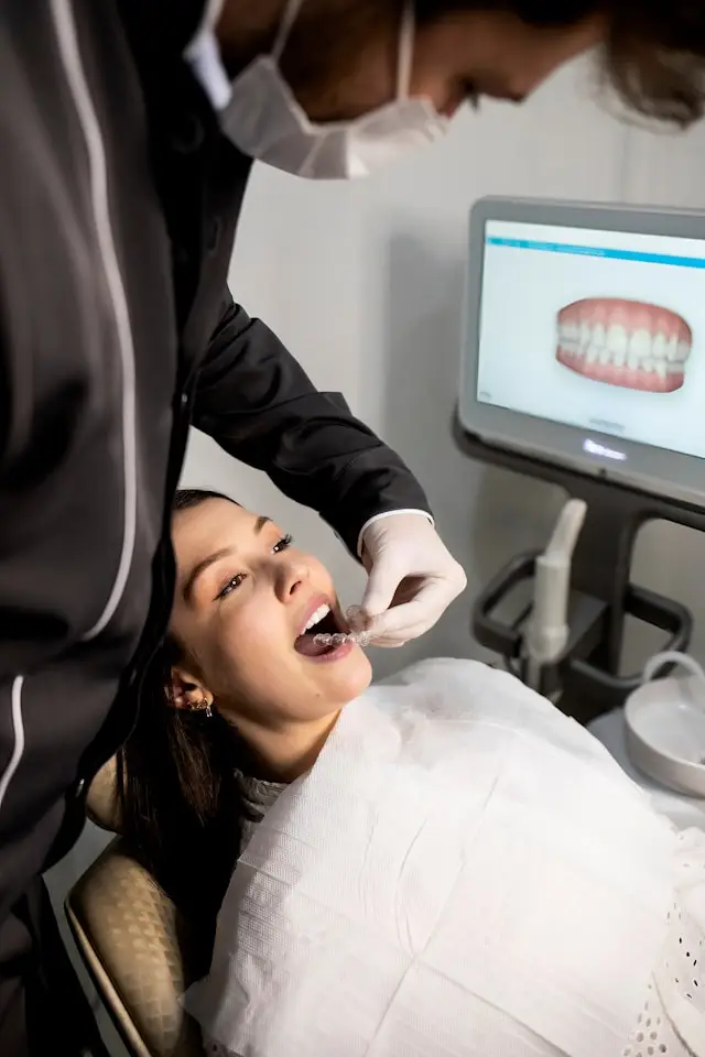 Clinician fitting a clear aligner into a patient's mouth beside a digital scan monitor