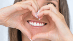 Close-up of a smiling woman framing her white teeth with hands in heart shape