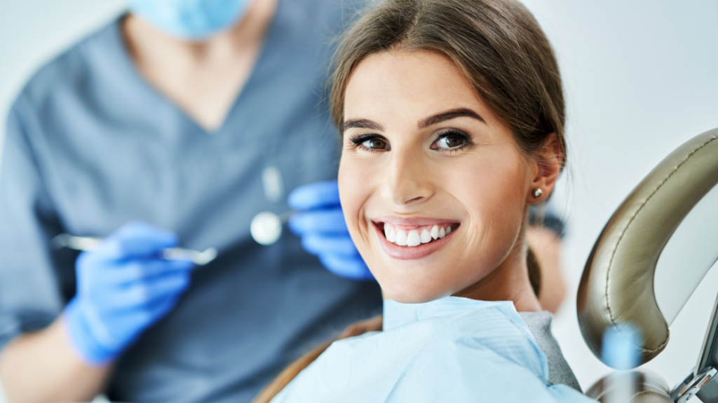 Smiling woman in a dental chair with a clinician in blue gloves behind her