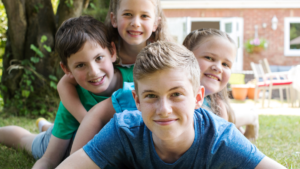 Group of four smiling kids piled on top of each other on a backyard lawn