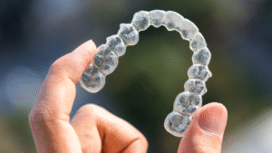 Hand holding a clear plastic Invisalign aligner tray outdoors
