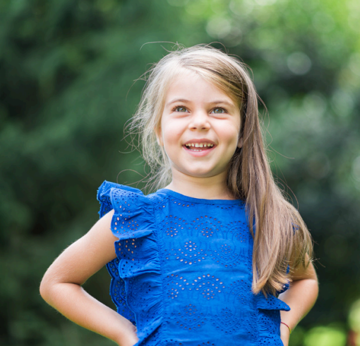 Smiling young girl in a blue ruffled top standing outdoors with hands on hips